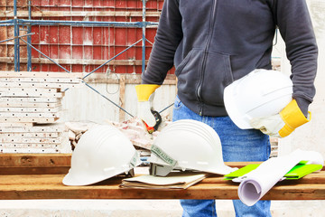 engineering hand holding white safety hat and paper plan blueprint on wood table in working construction site housing building with copy space add text
