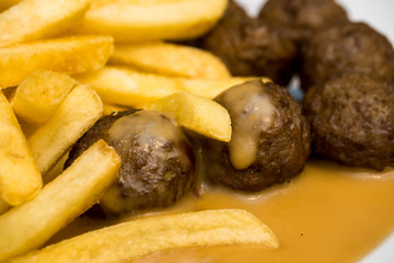 Delicious meatballs with peas, sauce and french fries in a white dish. Close-up. Shallow depth of field.