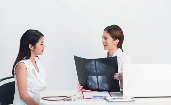  Female doctor holding  the Mammogram film image and give advice her patient in consulting room.