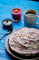 Appetizing pie with a large layer of pink cream. Dessert decorated with caramel stars. A cup of tea, jam and a candle for a romantic tea party. Blue wooden table and black teaspoon.