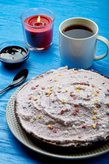 Appetizing pie with a large layer of pink cream. Dessert decorated with caramel stars. A cup of tea, jam and a candle for a romantic tea party. Blue wooden table and black teaspoon.