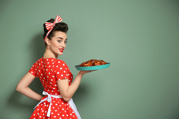 Funny young housewife with homemade pastry on color background