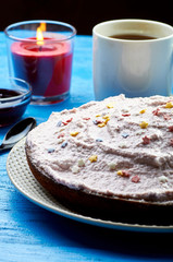 Appetizing pie with a large layer of pink cream. Dessert decorated with caramel stars. A cup of tea, jam and a candle for a romantic tea party. Blue wooden table and black teaspoon.