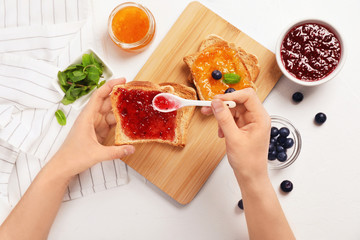 Woman spreading sweet jam on toast over table, top view