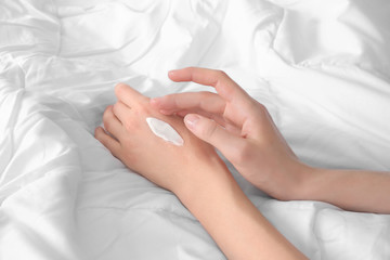 Obraz na płótnie Canvas Young woman applying cream onto hands, indoors