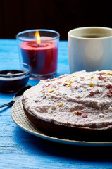 Appetizing pie with a large layer of pink cream. Dessert decorated with caramel stars. A cup of tea, jam and a candle for a romantic tea party. Blue wooden table and black teaspoon.