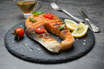 Slate plate with tasty salmon steak on grey background