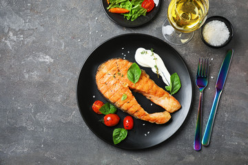 Plate with tasty salmon steak and wine on grey background