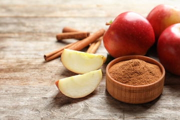 Fresh apples with cinnamon sticks and powder on wooden table