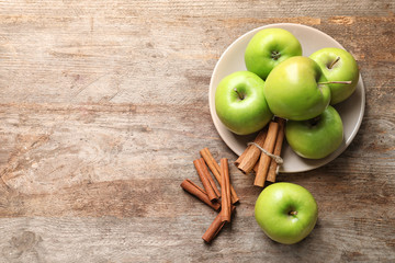 Fresh apples and cinnamon sticks on wooden table, top view