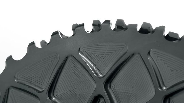Black oval bicycle chainring gear rotating at white background, strong close up with visible details of structure