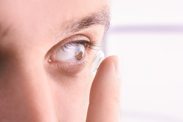 Young man putting contact lens in his eye, closeup