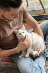 Young man with cute cat sitting on floor at home