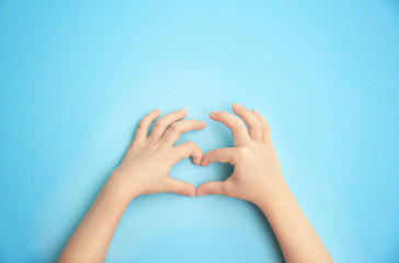 Child holding hands in shape of heart on color background. Happy Mother's Day