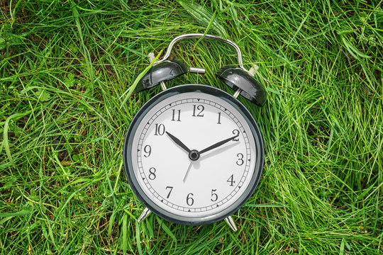 Alarm Clock On Green Grass, Outdoors. Time Change Concept