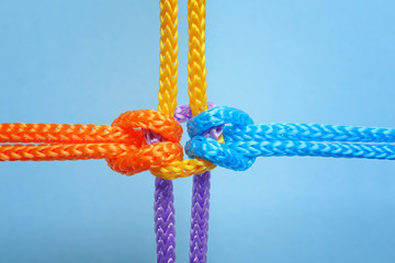 Different ropes tied together with knot on color background. Unity concept