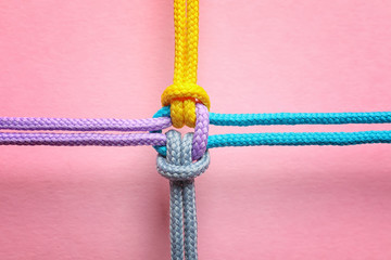 Different ropes tied together with knot on color background. Unity concept - obrazy, fototapety, plakaty