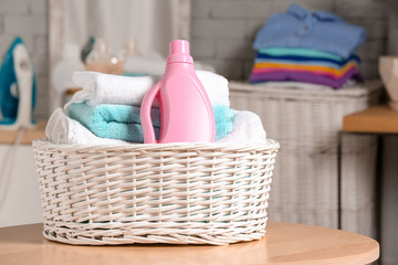 Laundry basket with clean towels and bottle of detergent on table