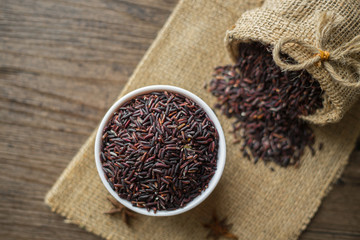 Healthy food background : Raw Rice berry in a white bowl and pouring by a bag  on the wooden table.