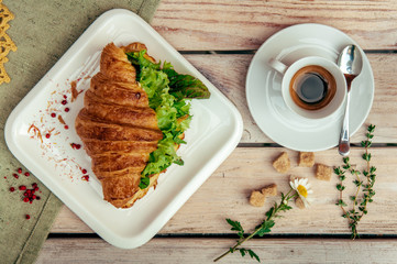 breakfast with green croissant, black coffee decorated with chamomile and brown shugar on wooden table.
