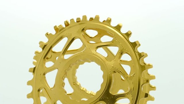 Golden oval bicycle chainring gear rotating at white background, strong close up with visible details of structure