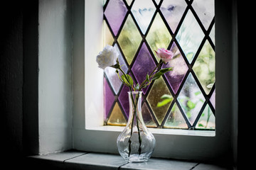 Colorful stained glass window with flowers in vase in the shadows