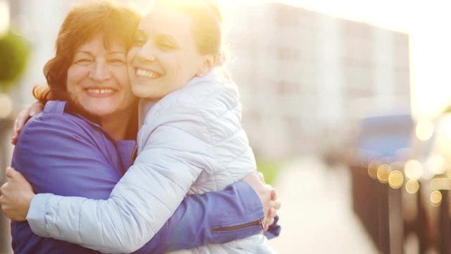 Happy mother and her aduit daughter. Women gently embrace and joyfully look at the camera. Family traditions. Mothers Day
