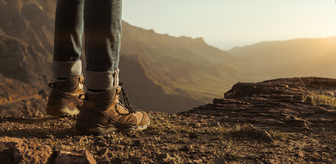 Close up of hikers boots enjoying sunset at the top of the mountains with copy space