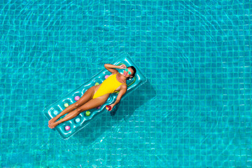 amazing beautiful girl in a yellow bikini air mattress swims in the pool of a luxury hotel, summer...