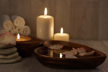 Fototapeta na wymiar Burning white candles and spa treatment set, water with rose petals and towels