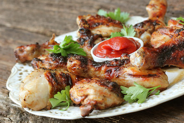 Grilled chicken legs on wooden table served on white plate with coriander