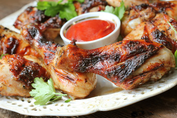 Grilled chicken legs on wooden table served on white plate with coriander
