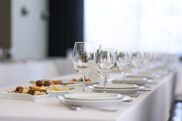 a row of crystal glasses and white plates on a festive table in a restaurant