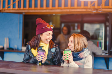 communication and friendship concept - smiling girls drinking coffee in outdoor cafe and smiling