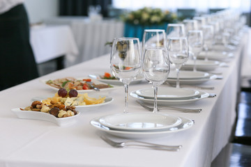a row of crystal glasses and white plates on a festive table in a restaurant