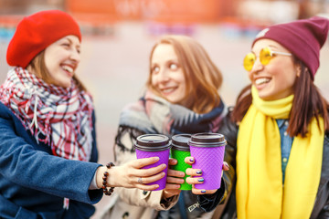 Three girls friends having fun outdoors and drinking coffee from paper cups