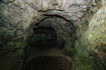 Obraz premium Beautiful cave. View from inside dark dungeon. Textured walls of cave. Background image of underground tunnel. Dampness inside cave. Light at end of tunnel.