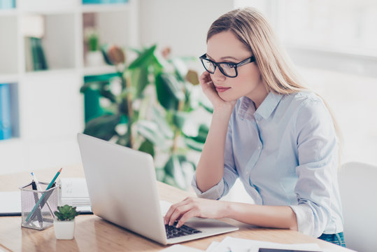 Portrait of smart agent, charming teacher, pretty woman, nice assistant in glasses working online on pc, using internet, looking at screen of laptop, sitting at desktop in work place, station