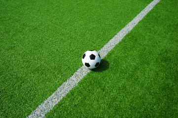 Klassischer Fussball schwarz weiss auf der Linie mit gr&uuml;nem Kunstrasen in der Sonne im Sommer