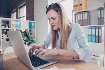 Portrait of nervous, stressed stylish woman with glasses on head looking at screen of computer typing quickly on keypad, searching important information online, she need to get in time