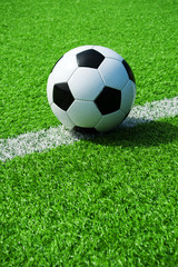 Fototapeta premium Klassischer Fussball schwarz weiss auf der Linie mit grünem Kunstrasen in der Sonne im Sommer