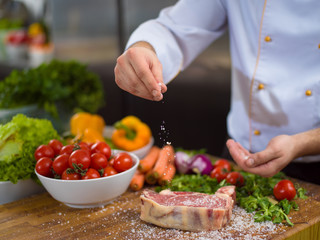 Chef putting salt on juicy slice of raw steak