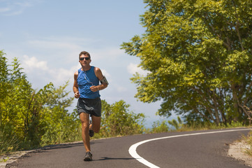 young attractive sport runner man training in asphalt road running workout a sunny Summer morning surrounded by trees and vegetation