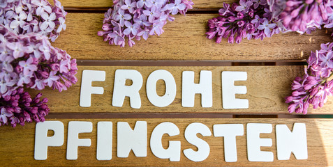 Frohe Pfingsten Wörter auf einem Holtbrett mit Flieder Blumenstrauß
