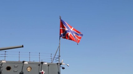 Russian navy flag on cruiser Aurora - historic revolution ship, waving in the wind against blue sky.