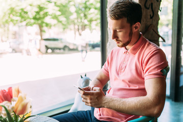 Young man sitting in cafe with laptop and phone, working, shopping online, hipster