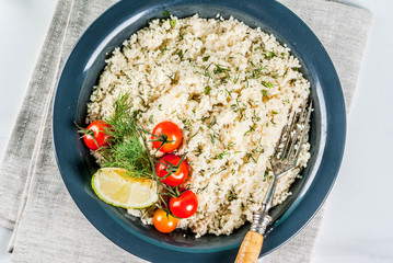 Light dietary food, couscous with tomatoes, lime and fresh herbs in dark bowl, white marble background