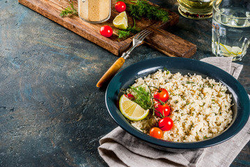 Light dietary food, couscous with tomatoes, lime and fresh herbs in dark bowl, dark blue background...