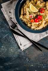 Classic italian pasta fusilli with pesto sauce, tomatoes, lime and fresh herbs in dark bowl, dark blue background  copy space