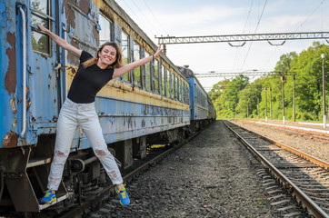 A young beautiful girl is standing on the step of an old railway carriage, a departing train